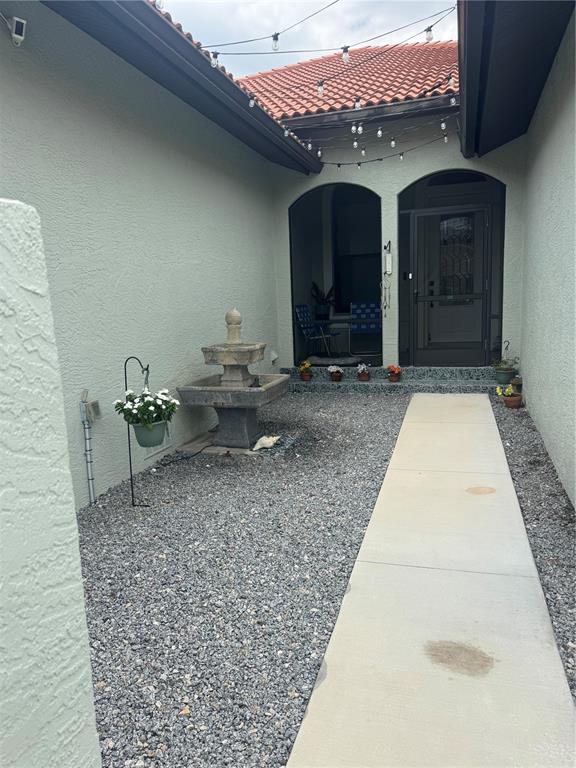 A concrete walkway leads to an arched entryway with a stone fountain in a courtyard — 408 TORTUGA DRIVE, NOKOMIS, FL