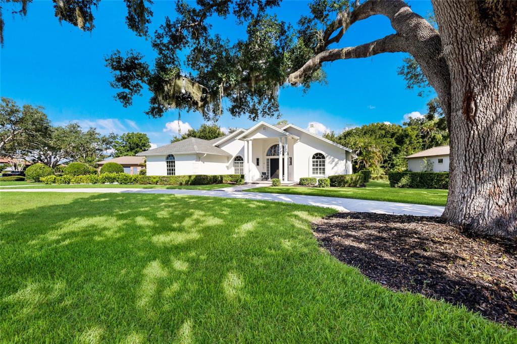 A white single-story house with a large oak tree in the foreground and green lawn — 3649 WILDERNESS BOULEVARD W, PARRISH, FL