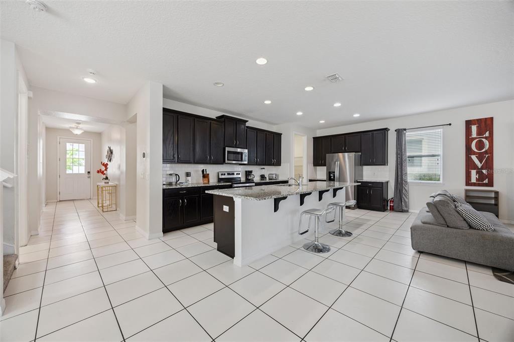 A kitchen with dark cabinets, granite countertops, and a center island opens to a living area — 9008 SUNSHINE RIDGE LOOP, KISSIMMEE, FL