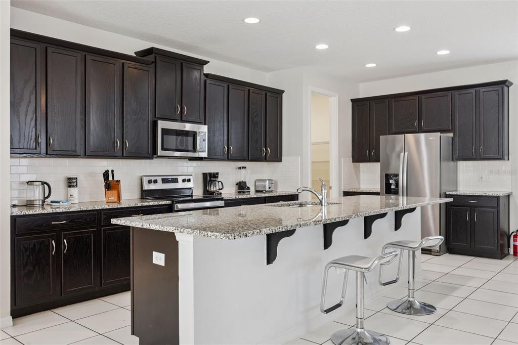 A kitchen with dark wood cabinets, granite countertops, a center island, and stainless steel appliances — 9008 SUNSHINE RIDGE LOOP, KISSIMMEE, FL