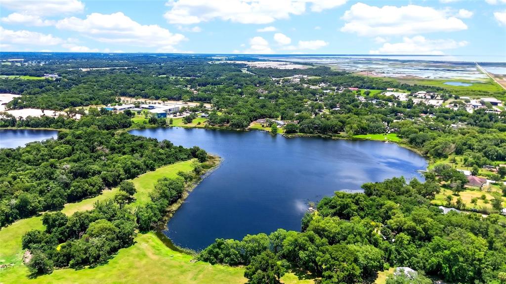 An aerial view shows a large lake surrounded by dense trees and grassy fields — 4162 LAUGHLIN ROAD, MOUNT DORA, FL