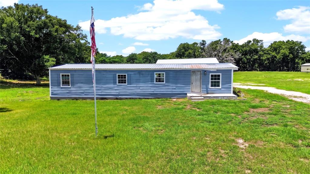 A blue single-story house with a metal roof stands in a grassy field — 4162 LAUGHLIN ROAD, MOUNT DORA, FL