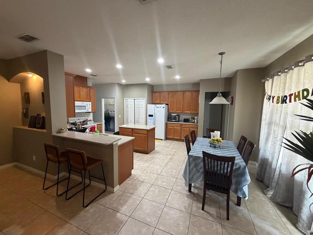 An open-concept kitchen and dining area features wood cabinets, tile flooring, and a breakfast bar — 430 MERLOT DRIVE, OCOEE, FL
