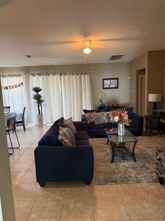 A living room features a dark blue sofa, a glass coffee table, and tile flooring — 430 MERLOT DRIVE, OCOEE, FL