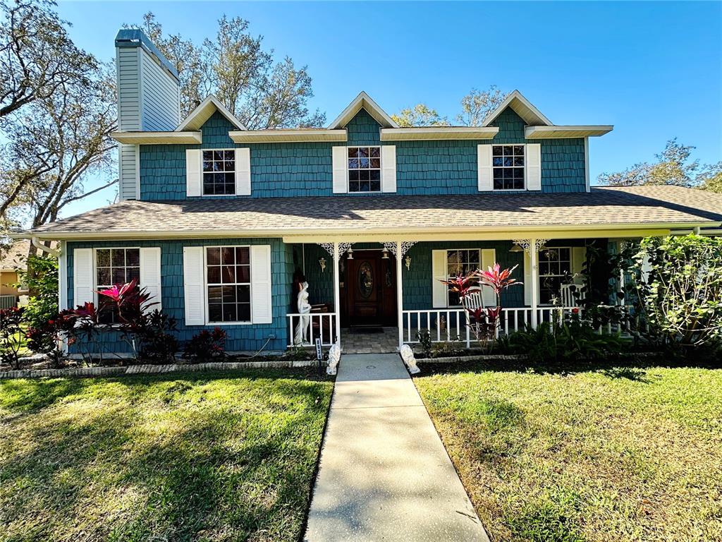 A two-story blue house with white shutters, a front porch, and a concrete walkway — 8834 WHISPERING OAKS TRAIL, NEW PORT RICHEY, FL