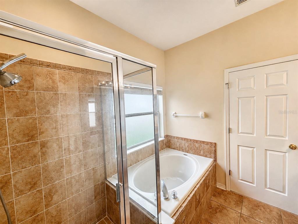 A bathroom features a tiled walk-in shower, a corner soaking tub, and a white door — 2240 FLORIDA SOAPBERRY BOULEVARD, ORLANDO, FL