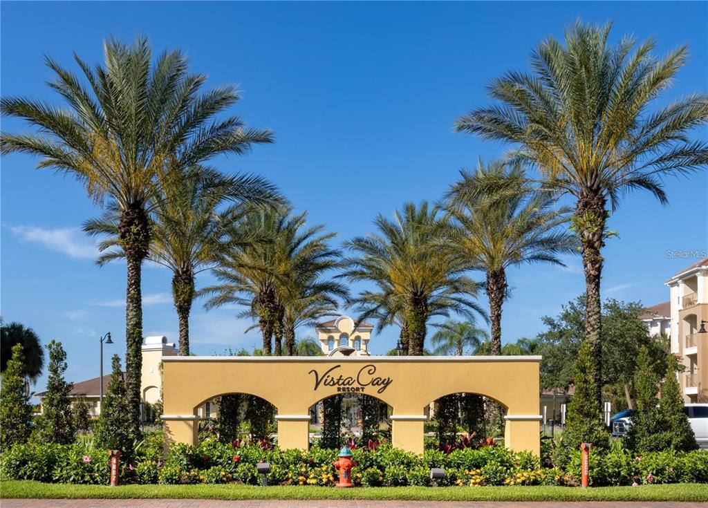 A yellow stucco entrance sign for Vista Cay Resort stands before several tall palm trees — 5048 SHOREWAY LOOP UNIT 20404, ORLANDO, FL