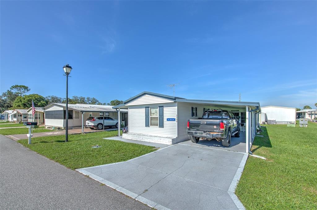 A white mobile home features a carport, a motorcycle, and a mailbox in the front yard — 5309 MONTEGO DRIVE, ZEPHYRHILLS, FL