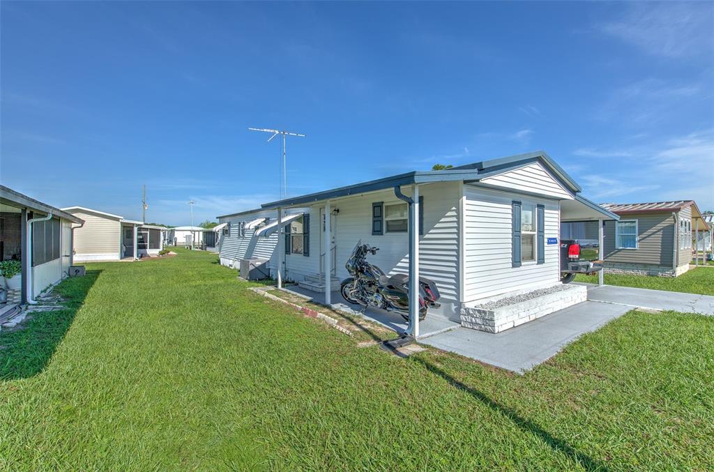 A white mobile home with a covered porch and a motorcycle parked in front — 5309 MONTEGO DRIVE, ZEPHYRHILLS, FL