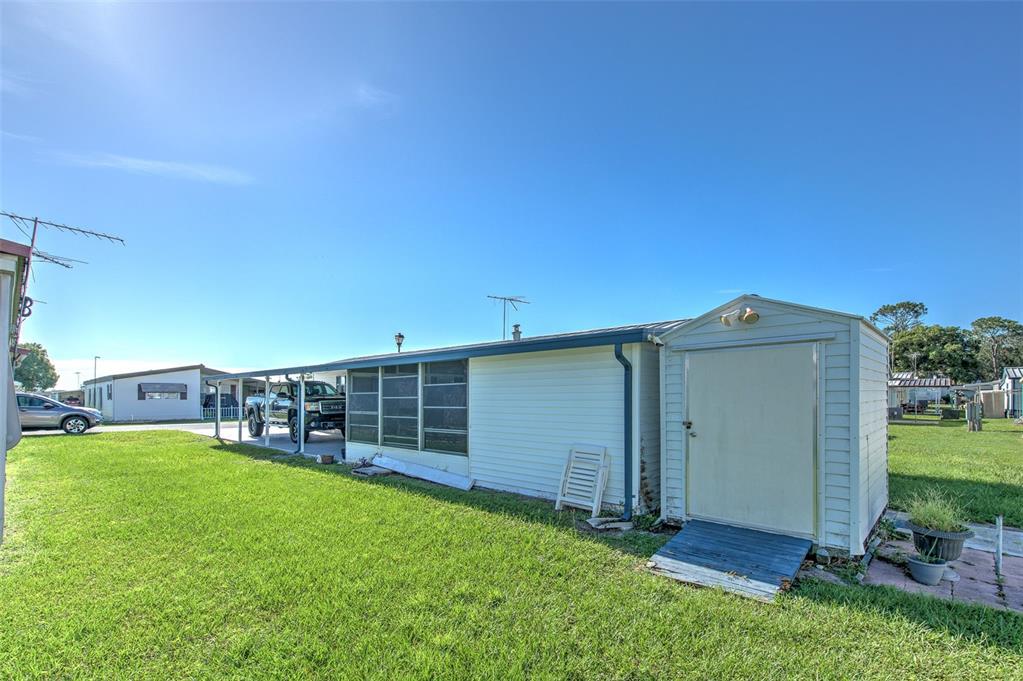 The exterior of a mobile home features a white storage shed and a covered carport — 5309 MONTEGO DRIVE, ZEPHYRHILLS, FL