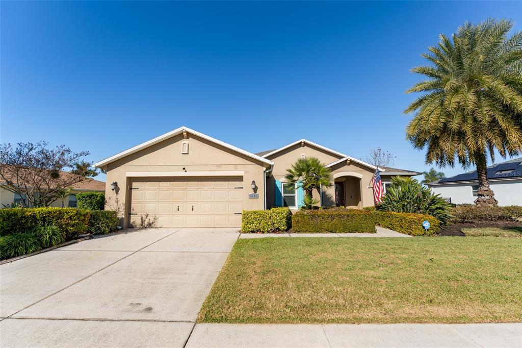 A single-story suburban house with a tan stucco exterior, a two-car garage, and a palm tree — 5431 SANDY SHELL DRIVE, APOLLO BEACH, FL