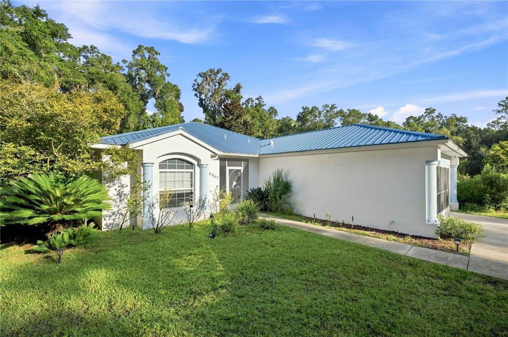 A single-story house with a blue metal roof and white stucco exterior sits on grass — 10062 SW 190TH COURT, DUNNELLON, FL