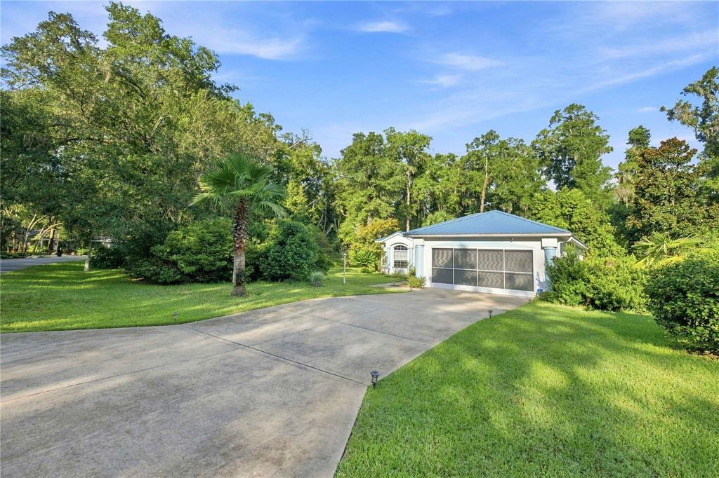 A concrete driveway leads to a house with a screened garage and a metal roof — 10062 SW 190TH COURT, DUNNELLON, FL