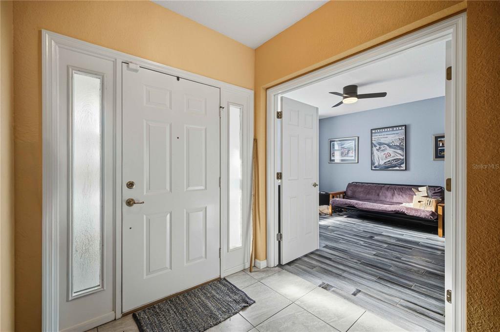 An entryway with a white front door and tiled floor leads into a room with wood-look flooring — 10062 SW 190TH COURT, DUNNELLON, FL