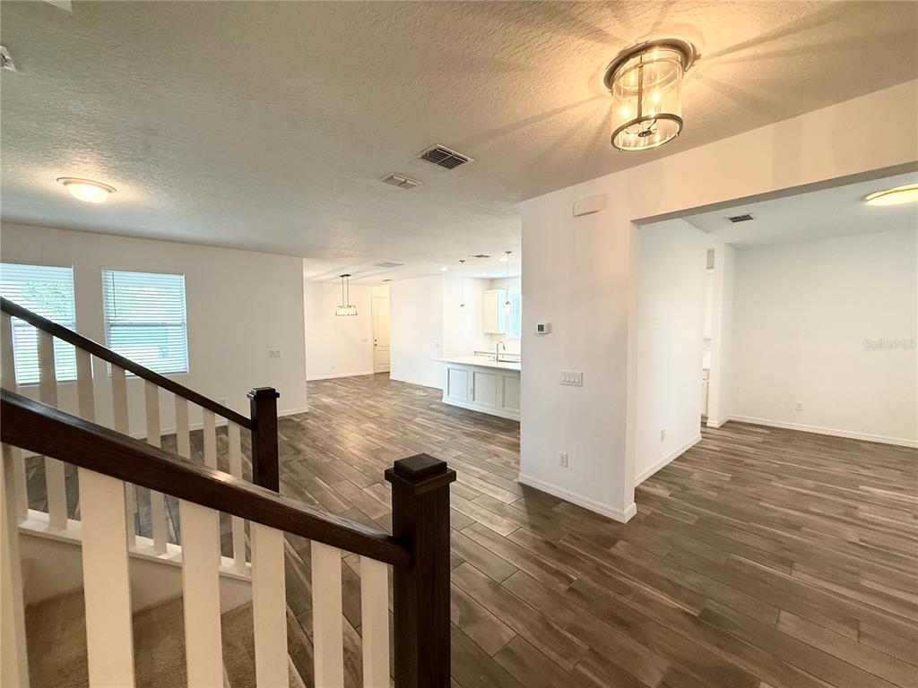 An interior view shows a staircase, wood-look tile flooring, and an open-concept kitchen area — 15124 LEMON PEEL ALLEY, WINTER GARDEN, FL