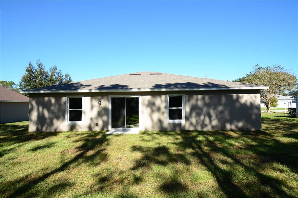 The exterior rear view of a single-story house features a sliding glass door and windows — 93 PANORAMA DRIVE, PALM COAST, FL