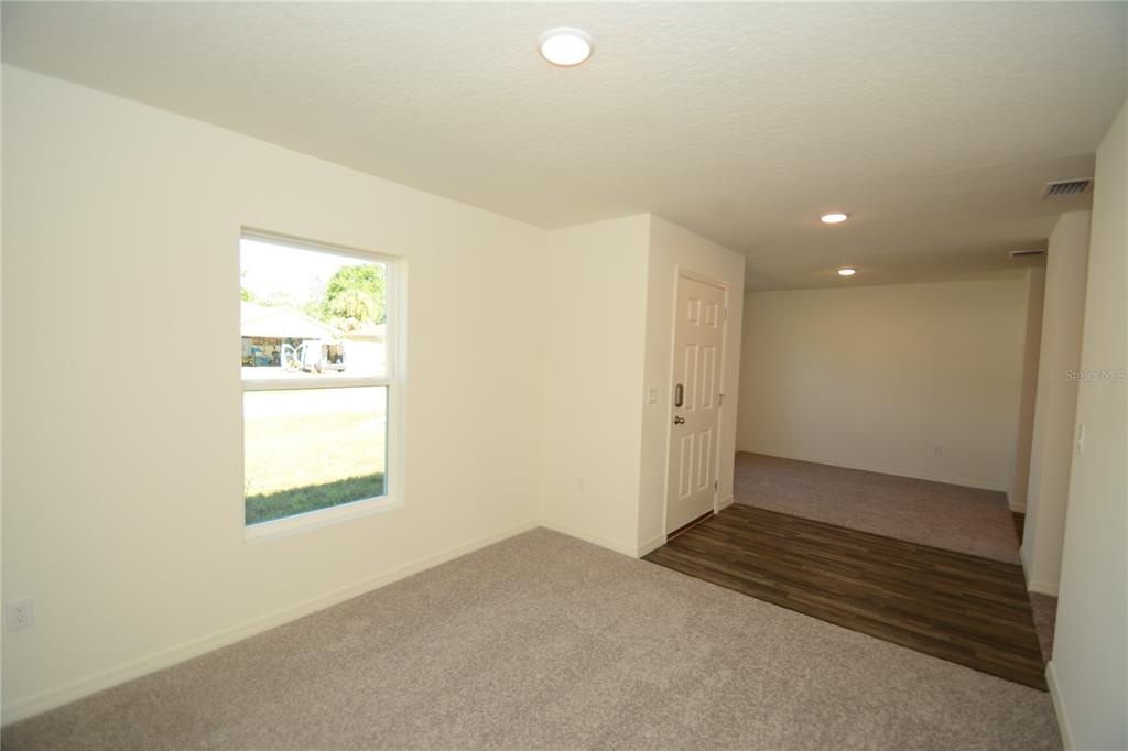 A room with beige carpet, a window, and a doorway leading to a carpeted area — 93 PANORAMA DRIVE, PALM COAST, FL