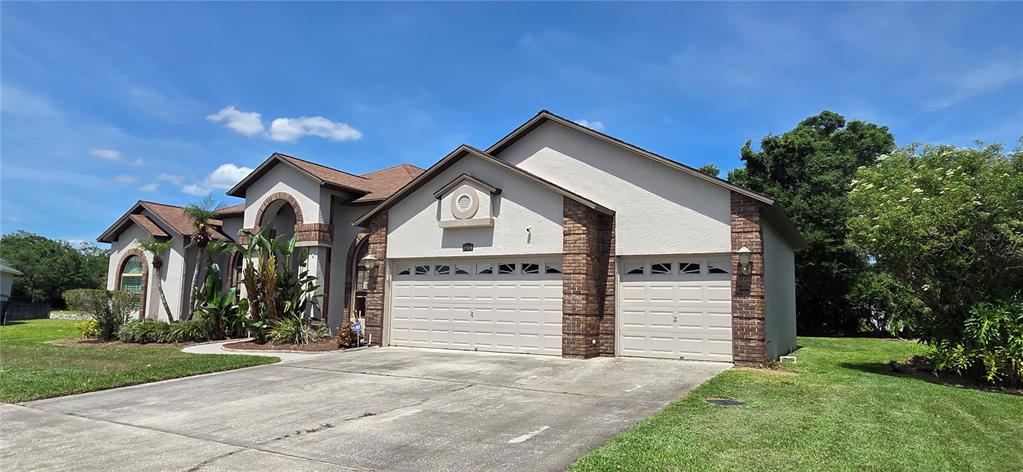 A single-story house with a beige stucco exterior, brick accents, and a three-car garage — 3904 HIDDEN SPRING PLACE, VALRICO, FL