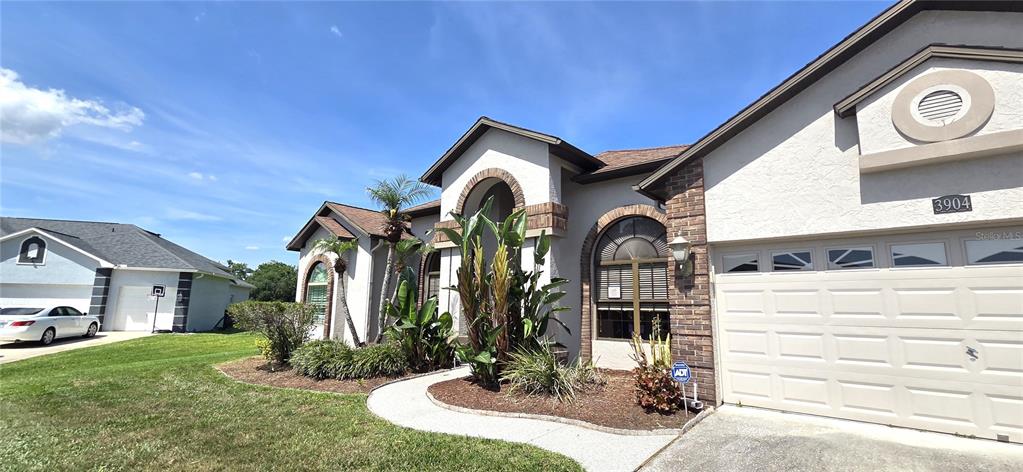 A single-story house exterior features a beige stucco facade, brick accents, and a garage — 3904 HIDDEN SPRING PLACE, VALRICO, FL