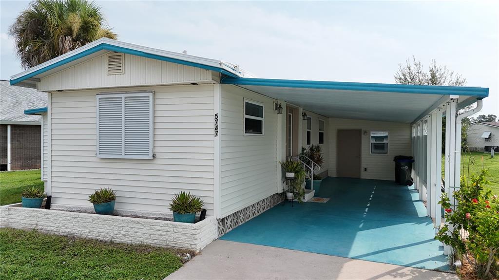 A single-story manufactured home with light siding, a blue-painted carport, and a white brick planter — 5747 HOLIDAY PARK BOULEVARD, NORTH PORT, FL