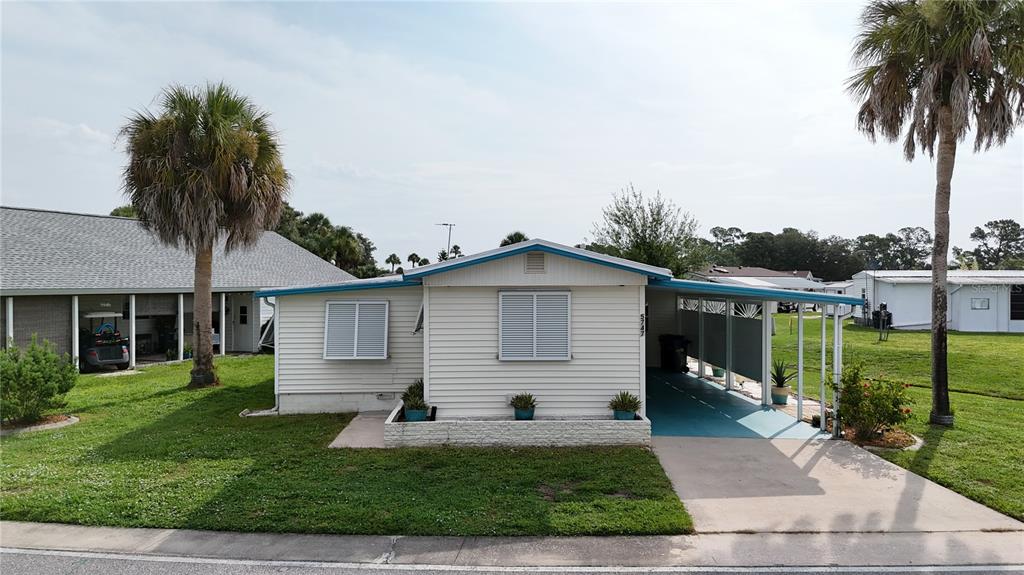 A single-story mobile home features white horizontal siding, a carport, and two palm trees — 5747 HOLIDAY PARK BOULEVARD, NORTH PORT, FL