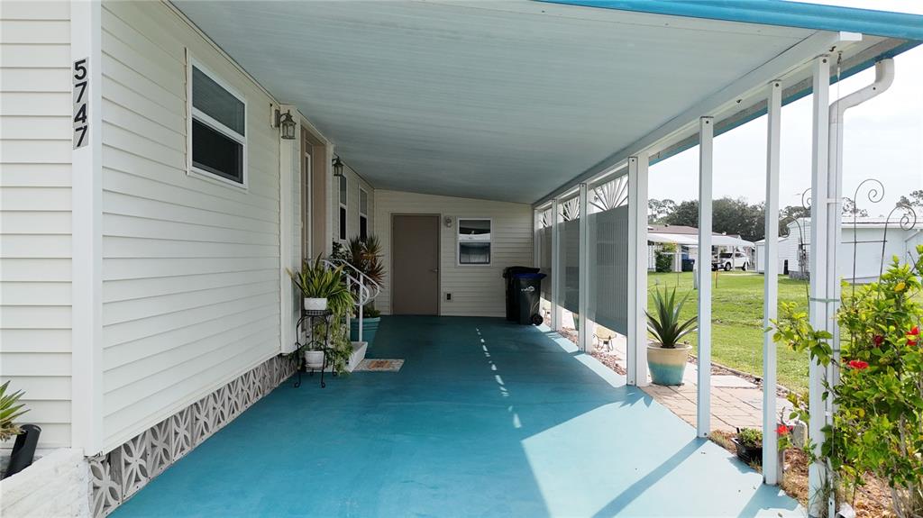 A covered carport with a blue floor leads to the entrance of a mobile home — 5747 HOLIDAY PARK BOULEVARD, NORTH PORT, FL