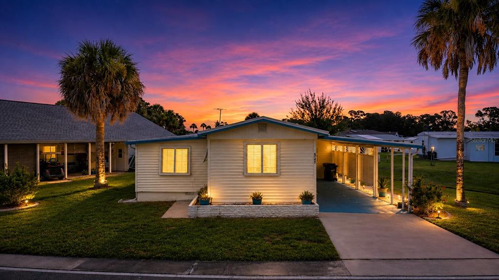 A single-story house with light siding, a carport, and palm trees under a sunset sky — 5747 HOLIDAY PARK BOULEVARD, NORTH PORT, FL