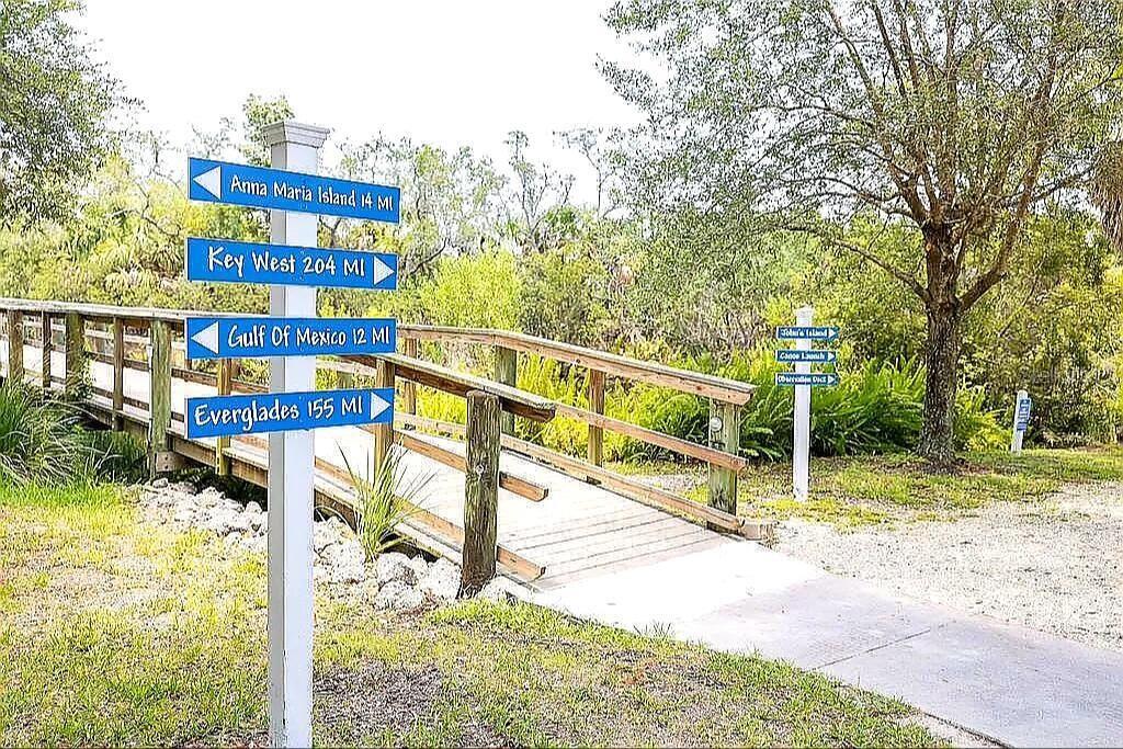 A wooden footbridge leads to a nature trail with directional signs in a park setting — 5662 WHITEHEAD STREET, BRADENTON, FL