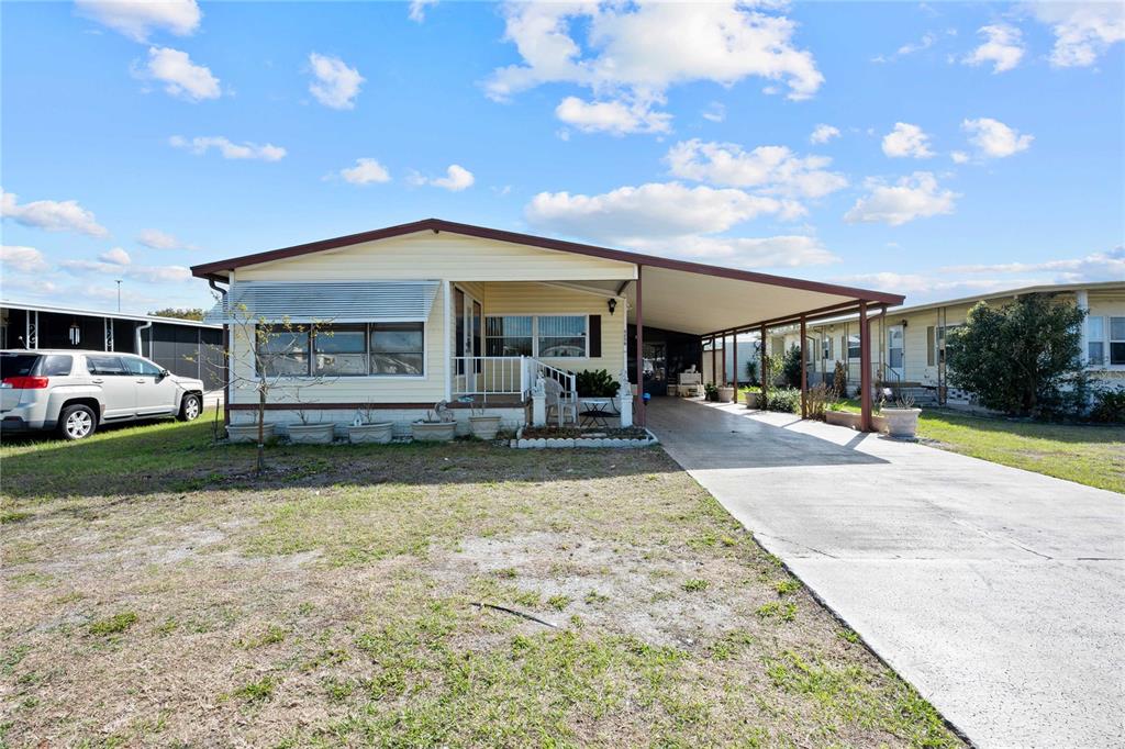 A yellow manufactured home with a concrete driveway and an attached carport under a sky — 5250 DEAN DAIRY ROAD, ZEPHYRHILLS, FL