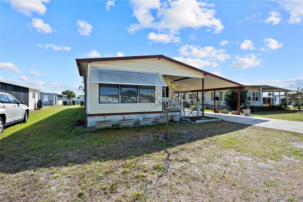 A yellow mobile home features a covered carport, a front porch, and concrete flooring — 5250 DEAN DAIRY ROAD, ZEPHYRHILLS, FL