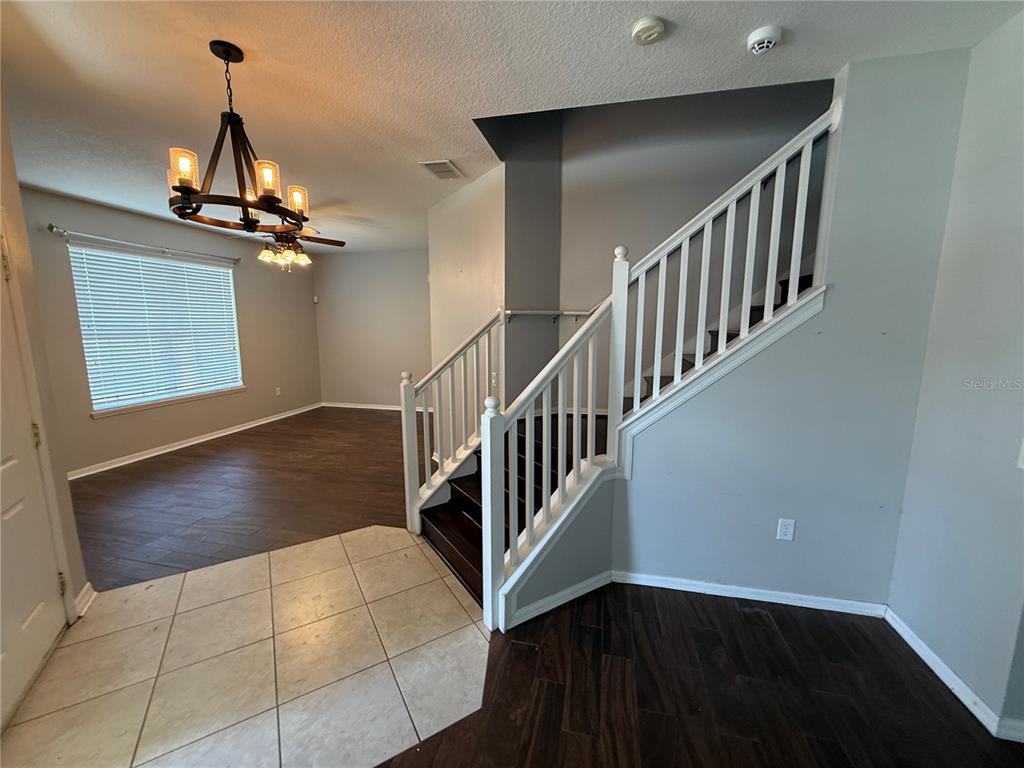 An entryway features tile flooring, a dark wood staircase with white railings, and a chandelier — 2260 TRADEWINDS DRIVE, KISSIMMEE, FL