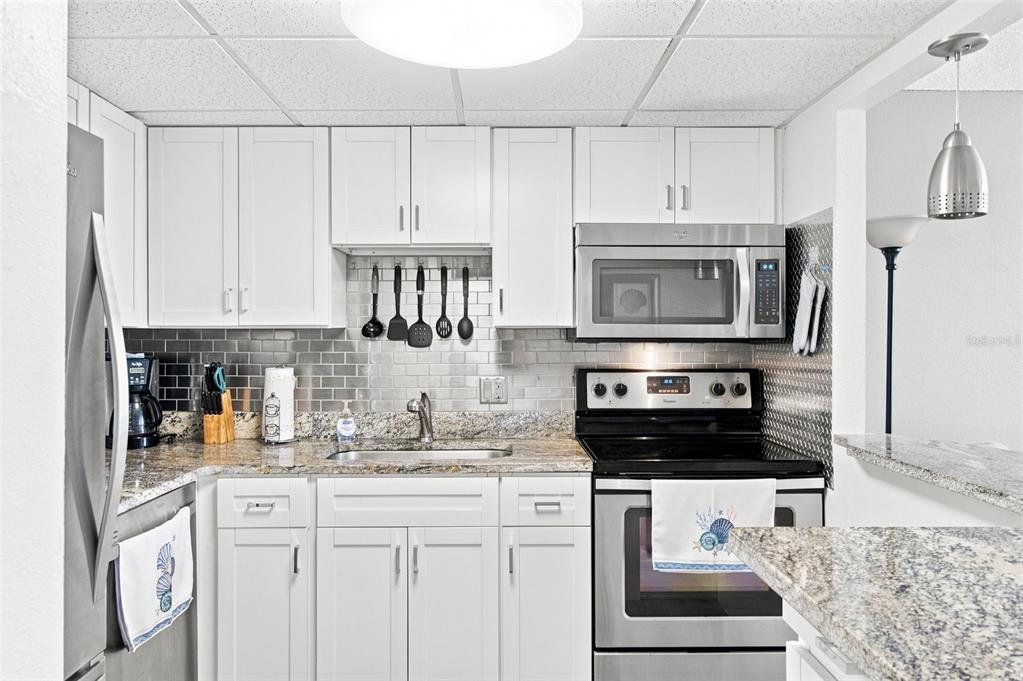A kitchen features white cabinets, granite countertops, a gray subway tile backsplash, and stainless appliances — 935 N HALIFAX AVENUE UNIT 604, DAYTONA BEACH, FL