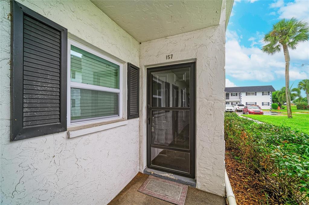 An exterior view of a residential unit entrance with a storm door and window shutters — 303 47TH AVENUE DRIVE W UNIT 157, BRADENTON, FL