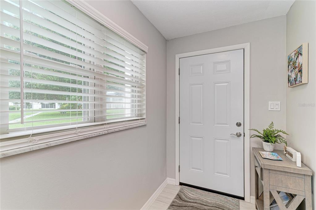 An entryway features a white front door, a window with blinds, and a small console table — 303 47TH AVENUE DRIVE W UNIT 157, BRADENTON, FL