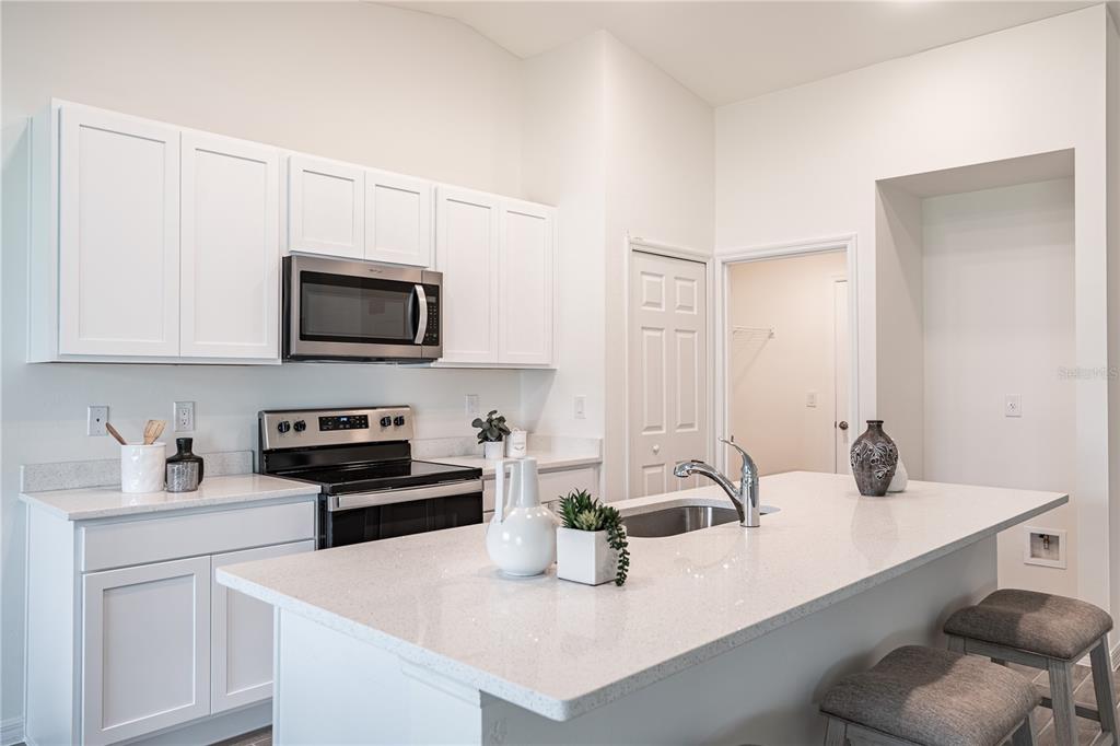 A modern kitchen features white cabinets, stainless steel appliances, and a large quartz-topped island — 1190 ZINNEA STREET, PORT CHARLOTTE, FL