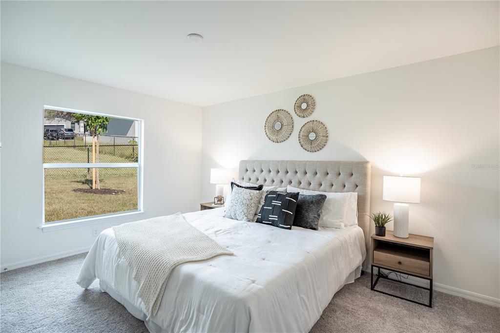 A bedroom features a tufted headboard, two nightstands with lamps, and a window overlooking a yard — 1190 ZINNEA STREET, PORT CHARLOTTE, FL