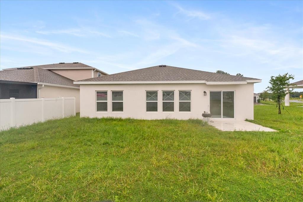 The rear exterior of a single-story house with a white stucco facade and a grassy yard — 4812 WORCHESTER DRIVE, KISSIMMEE, FL