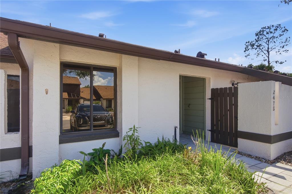The exterior of a white stucco home features a dark wooden gate and a window — 2475 TAHOE CIRCLE, WINTER PARK, FL