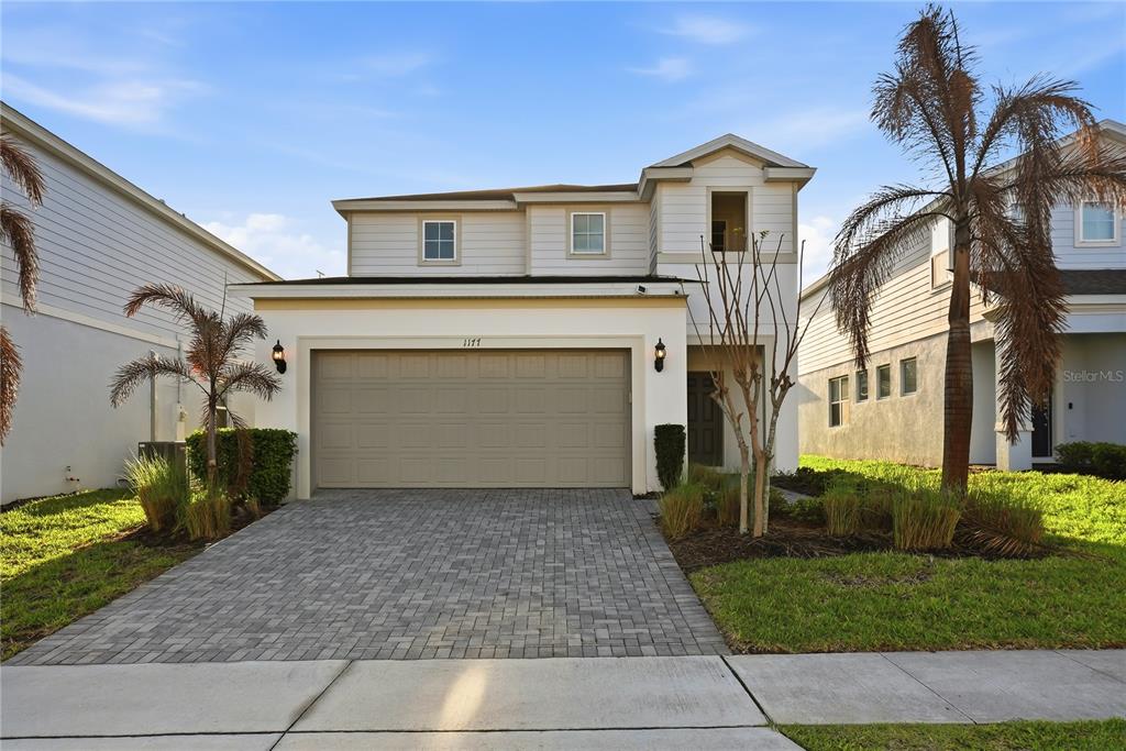 A two-story house with a beige garage, light-colored siding, and a paved driveway — 1177 ALOHA BOULEVARD, DAVENPORT, FL