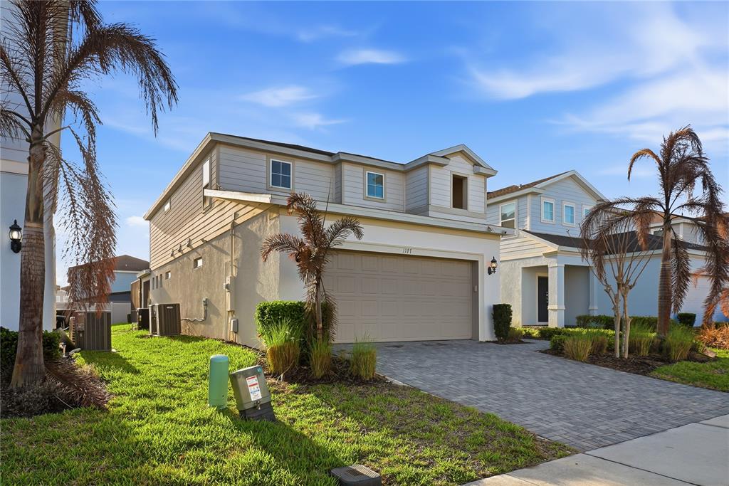 A two-story suburban house with a beige stucco exterior, a paved driveway, and palm trees — 1177 ALOHA BOULEVARD, DAVENPORT, FL