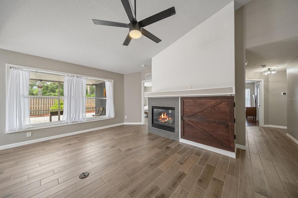 A living room features wood-look tile flooring, a fireplace with a barn-door cabinet, and windows — 11887 DUNSTER LANE, PARRISH, FL