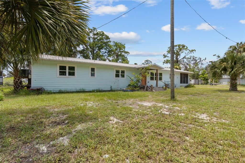 A single-story light blue house with a metal roof and an orange front door — 306 SE 256 STREET, SUWANNEE, FL