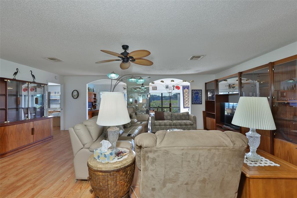 A living room features a beige leather sectional, patterned sofa, wood flooring, and wall mirrors — 2611 LANCASTER DRIVE UNIT 33, SUN CITY CENTER, FL