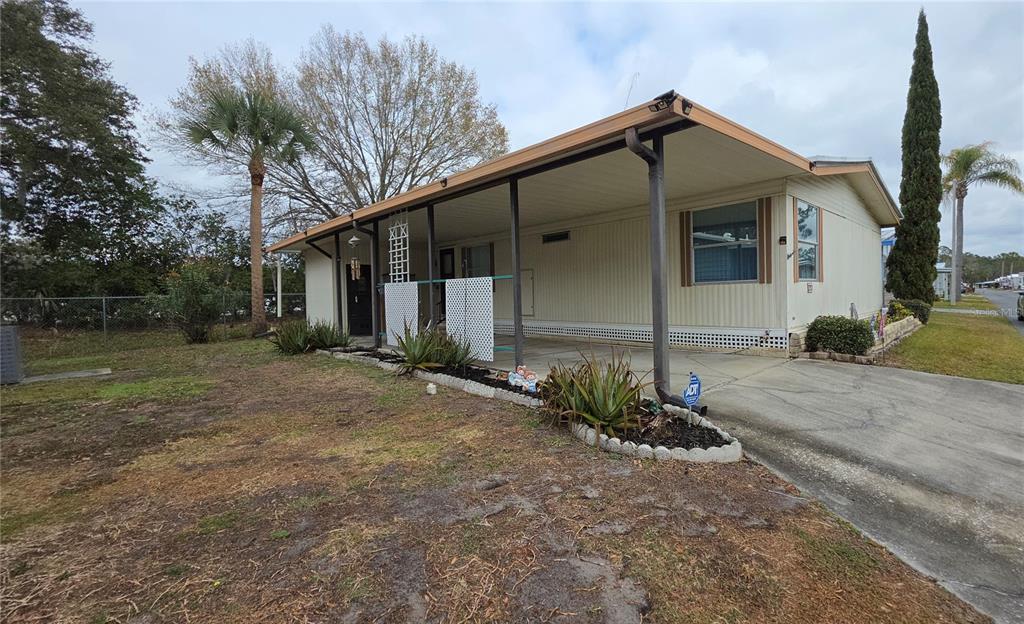 A single-story mobile home with a covered carport and a small landscaped garden bed — 252 PINEWOOD DRIVE, EUSTIS, FL
