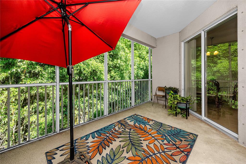 A screened-in balcony features a red umbrella, a patterned rug, and a view of trees — 894 LANTERN WAY, CLEARWATER, FL