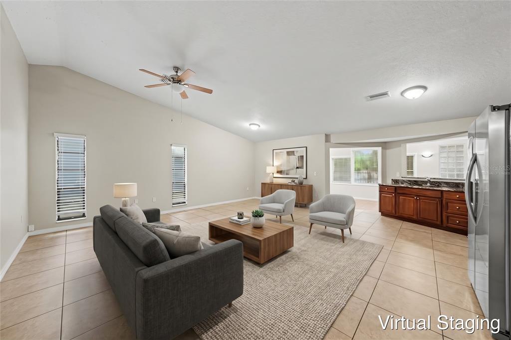A spacious living area with vaulted ceilings, tile flooring, and an adjacent kitchen counter area — 7623 BRAMBLEWOOD DRIVE, PORT RICHEY, FL