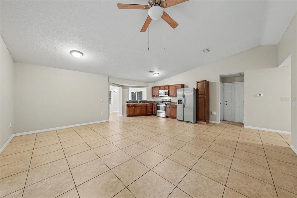 A kitchen with wood cabinets, stainless steel appliances, and tile flooring opens to a living area — 7623 BRAMBLEWOOD DRIVE, PORT RICHEY, FL