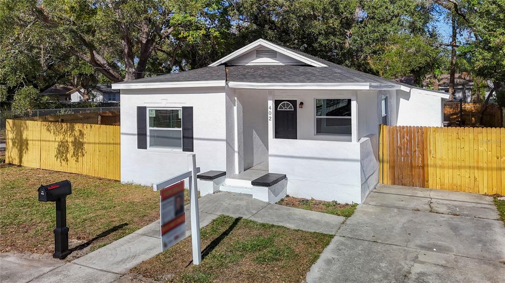 A small white house with a black front door, a concrete driveway, and wooden fencing — 402 E VIRGINIA AVENUE, TAMPA, FL