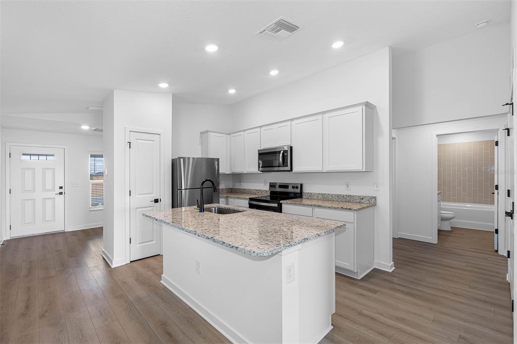 A kitchen features white cabinets, granite countertops, a center island, and wood-look flooring — 5215 CAP ROAD, BROOKSVILLE, FL