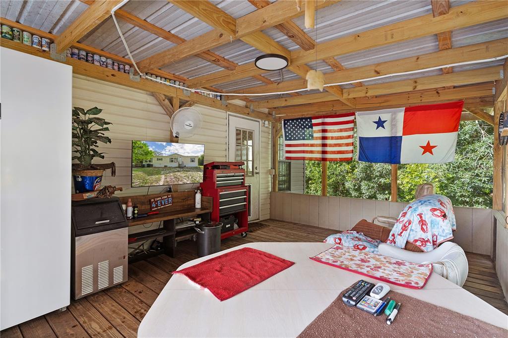 A covered outdoor patio features a television, tool chest, and flags hanging from wooden rafters — 6590 CR 631, BUSHNELL, FL